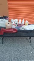 Overview of all cleaning supplies including vacuum, paper towels, bottles, and cloths on black outdoor table.