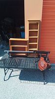 Wooden narrow shelf, wooden box shelf with compartments, black metal mesh rack and leather strap on metal frame base seen outdoors in sunlight