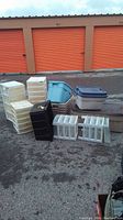 Overview of assorted storage bins and organizers of various sizes and colors, placed outdoors in front of orange storage unit doors.