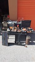 Wide view of various tools and racks displayed on the ground near an orange wall, including drill, metal racks, toolboxes, and small containers.