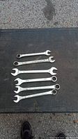 Lot of six combination wrenches laid out on a black surface outdoors, showing full wrenches and general condition.