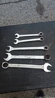 Top view of 5 metal combination wrenches arranged flat on black surface showing different sizes and ends.