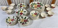 Overview of dinnerware collection showing multiple plates and cups with hand painted floral designs.