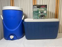 Full lot including blue cylindrical Coleman water cooler, blue rectangular Coleman cooler, and boxed Texsport single burner propane stove