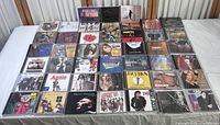 Overview image of approximately 40 music CDs displayed on a bed surface showing album covers and cases.