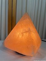 Front angled view of pyramid shaped pink salt lamp glowing warmly with visible textured crystalline salt surface.