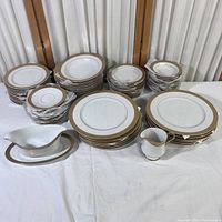 Full set arranged showing plates, bowls, saucers, gravy boat, and cream pourer with gold rim accents on white china.