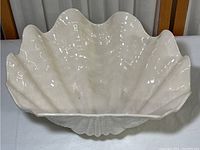 Top and side view of the off-white scallop shell ceramic dish showing the glossy glazed finish and shell details.
