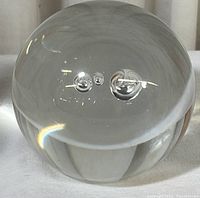 Front-facing photo of the spherical clear glass paperweight highlighting three controlled bubbles inside.