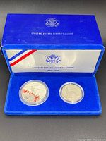 Blue velvet presentation box showing two silver coins in plastic holders with United States Liberty Coins branding and Ellis Island dates 1986-1986.