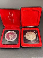 Two Canadian silver dollar coins in their original red velvet display boxes, each in a protective capsule.