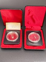 Two Canadian silver dollars in black protective holders inside red velvet presentation boxes, one box includes an inspection card.