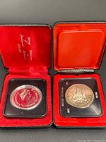Two Canadian silver dollar coins in their original black and red presentation boxes, viewed from above.