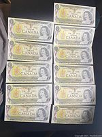 Front sides of eleven Canadian $1 bills arranged in two columns on a dark surface