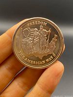 Obverse side of the Johnson Matthey silver coin depicting a settler family, American flag with 13 stars, and text 'FREEDOM' and 'THE AMERICAN WAY'.