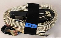 Coiled ratchet strap showing the metal ratchet mechanism and one end hook, secured with a black Velcro strap and a small blue tag.