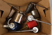 Top view of eight metal oil cans of various colors and designs inside a cardboard box
