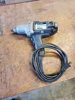 Side view of the B&D electric impact wrench showing the Black & Decker label and attached power cord coiled on table surface.