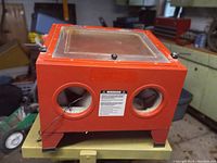 Front view of red benchtop sandblasting cabinet with two glove ports and viewing window on top.