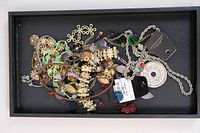 Top-down view of multiple costume jewelry pieces including necklaces and a bracelet in a black tray