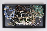 Top-down view of varied costume jewelry pieces in a tray showing necklaces and bracelets made of beads and metal chains in assorted colors.