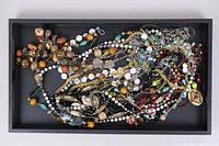 Photo showing a black tray filled with tangled costume jewelry, mostly necklaces and chains of mixed materials and colors.