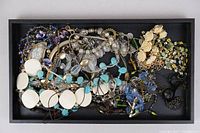 Photo showing a tray filled with assorted costume jewelry pieces including bead necklaces, floral bracelets, and mixed metal chains.