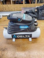 Front side view of Delta air compressor showing brand logo, 2-gallon tank label, and the unit's structure and handle.