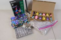 Overview photo showing the box of LED holiday lights, bags of confetti and beads, box of plastic Easter eggs, and snowflake ornament.