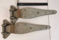 Top view of a large metal hinge on a flat surface with measuring ruler indicating length around 12 inches.