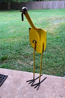 View of the full yellow metal bird sculpture standing on a concrete patio with grass in background.