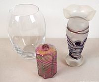 Lot of three glass items: a clear oval vase, iridescent oil lamp bottle, and frosted vase with purple swirls.