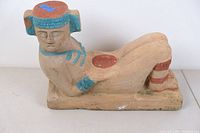 Side view of the seated clay figure showing painted details on head, arms, and legs.