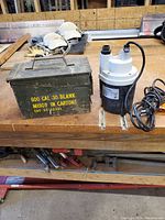 Photo of the utility pump and metal ammunition-style box placed on a workbench with some tools in the background.