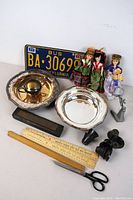 Overview photo showing license plate, dolls, silverplate bowl, glass candle holder, wooden ruler, scissors, black fittings, magnifying glass.