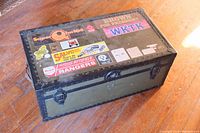 Full view of closed WWII footlocker showing black metal trim and stickers on lid