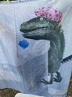 Shower curtain with a realistic dinosaur wearing a pink polka dot shower cap, folded and hanging to show full design.