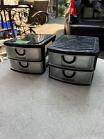 Two black plastic small storage units with multiple translucent drawers shown side by side on an outdoor table.