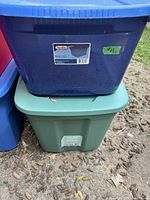 Photo showing stacked blue and green plastic totes outdoors with visible dirt and wear.