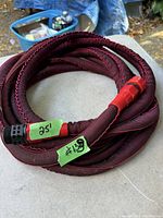 Coiled maroon fabric braided garden hose showing both ends with plastic connectors and tape labels.