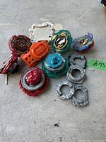A collection of Beyblade Burst tops, string launchers, Beyblade rings, and stadium accessory laid out on a light surface.