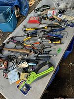 Wide view of table filled with assorted tools and hardware showing various hand tools arranged randomly, including hammers, saw, pliers, and clamps.