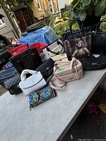 Full lot of 9 purses and a wallet on a table, showing variety of styles and colors