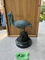 Front view of bronze pelican sculpture on round marble base with wood background