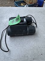 Top and side view of Bushnell compact binoculars showing rubberized grips, Bushnell branding and attached neck strap.