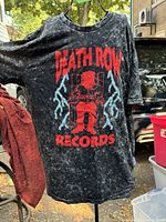 Black vintage Death Row Records T-shirt with red graphic depicting seated figure in electric chair with lightning bolts. Shows faded, distressed fabric indicative of age and wear.