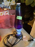Tall glass lava lamp with purple wax and blue tinted liquid, standing on marbled blue and white base, with power cord visible.