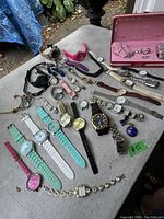 Photo shows entire lot of watches laid out on table including variety of styles and colors.