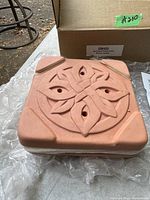 Top view of square pink ceramic flower press with carved ornamental floral design on top and packaging box behind it.