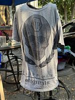 Full view of gray Philipp Plein T-shirt hanging, showing skull and laurel leaf graphic and text at bottom front.